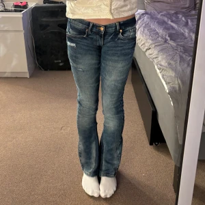 Blå bootcut jeans - Snygga blå bootcut jeans med slitna detaljer. De har en klassisk femficksdesign och en låg midja. Midjemåttet rakt över är 34cm och inerbenslengden är 75. Byxorna är veldigt stretchiga. 