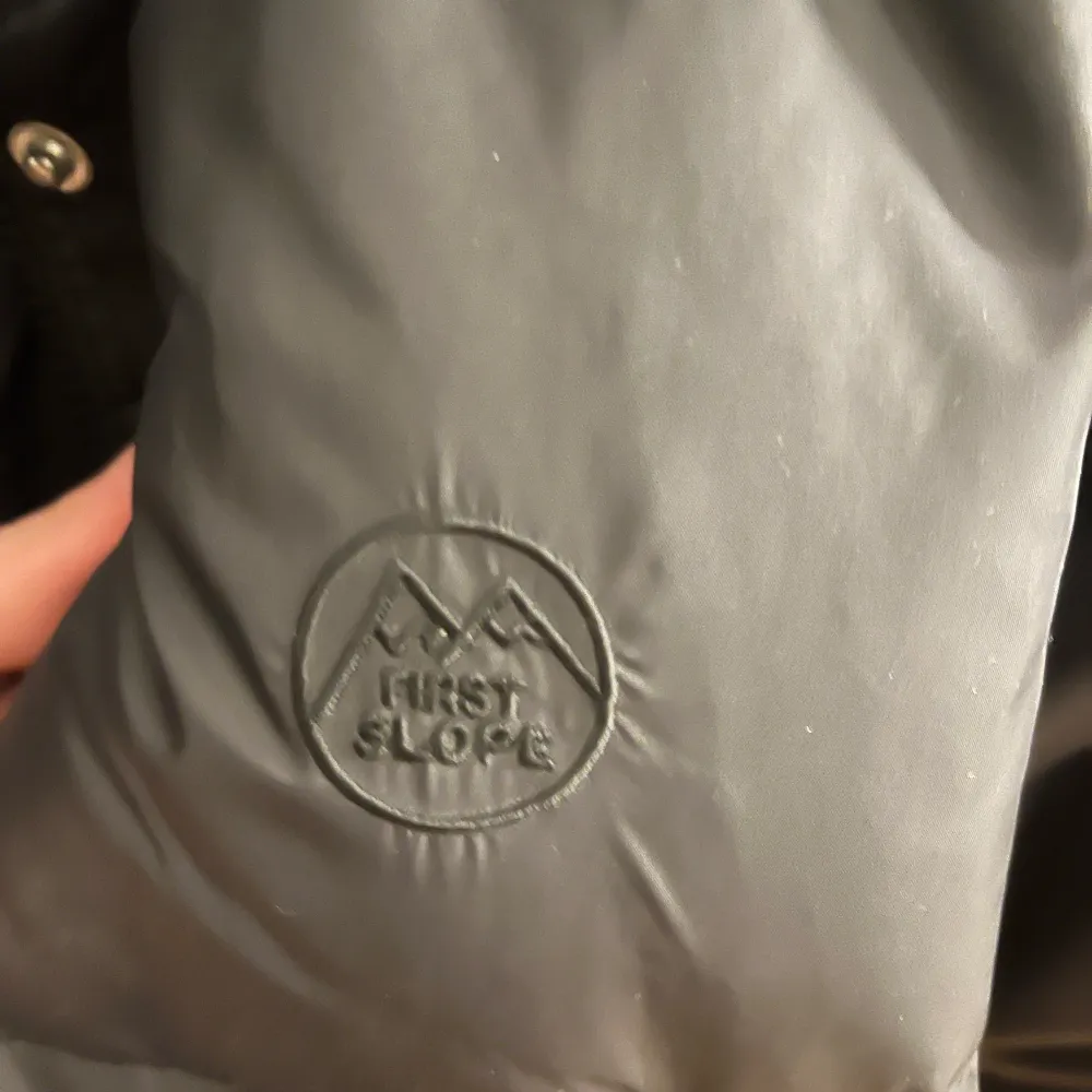 Säljer en svart pufferjacka från First Slope. Jackan har en dragkedja framtill och är perfekt för kyligare dagar. Den är långärmad och har en stilren design med logotyp på bröstet. Har en skada (sista bilden). Passar perfekt för vinterns äventyr! 🖤. Takit.