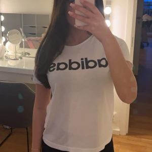 Vit t-shirt från Adidas - Säljer en klassisk vit t-shirt från Adidas med deras ikoniska logga i svart på framsidan. T-shirten har en rund halsringning och korta ärmar, perfekt för en avslappnad stil.