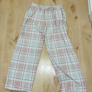 Rutig byxa i beige och vit - Snygga och bekväma byxor med rutigt mönster i beige och vit. De har en loose passform och är perfekta för en avslappnad stil. Byxorna har elastisk midja för extra komfort.