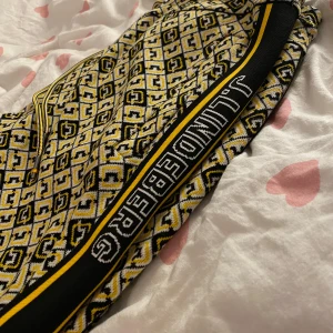 Mönstrade byxor från J.Lindeberg - Snygga byxor från J.Lindeberg med ett unikt geometriskt mönster i svart och gult. Byxorna har en normal passform och är utrustade med snörning i midjan för justerbarhet. Sidopaneler med J.Lindeberg-logga ger en sportig touch.