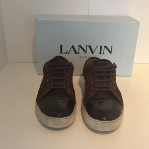 Bruna sneakers från Lanvin - Lanvins skor som är bruna realativt nya och nysydda. Skick 8/10.har deffekter som tappat en liten bit på sulan på baksidan och sidan på skon. Säljer skorna eftersom jag har ett par nya skor. Kommer med box dustbag och ett par nya snören. Kom gärna med förslag av priser. 