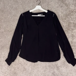 Svart blus från Vila - Elegant svart blus från Vila med v-ringning och långa ärmar. Perfekt för en stilren look. Tillverkad i ett mjukt material som ger en skön passform.