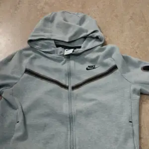 Säljer en grå hoodie från Nike i storlek 147-158 cm. Den har en dragkedja framtill och en huva för extra mys. Perfekt för träning eller chill dagar. Den är i bra skick och redo för en ny ägare!