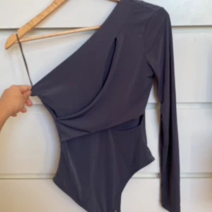 one shoulder cutout body - En fin grå body som jag har använt en gång. Den går ej att köpa längre. Ny pris 299kr.  Sista bilden är lånad.☺️