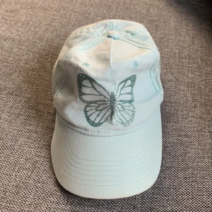 En blå keps med en blå glittrig fjäril  - Storlek 52-54  den e blå med en glittrig fjäril bra för sommaren 