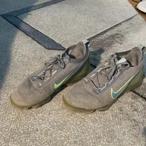 Säljer ett par grå Nike Vapormax sneakers i bra skick. De har en snygg design med en grön Nike-logga på sidan och snörning framtill. Perfekta för träning eller vardagsbruk! Ordinarie pris 2695 Storlek 45,5 passar även 45&46