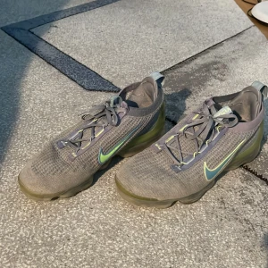Grå Nike Vapormax sneakers - Säljer ett par grå Nike Vapormax sneakers i bra skick. De har en snygg design med en grön Nike-logga på sidan och snörning framtill. Perfekta för träning eller vardagsbruk! Ordinarie pris 2695 Storlek 45,5 passar även 45&46