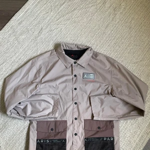 Beige jacka från Jordan x Paris - Säljer en snygg beige overshirt från Jordan x Paris. Den har en cool design med tryck på både fram- och baksidan. Den har knappar framtill och två stora fickor. Perfekt till hösten! Passar även storlek m