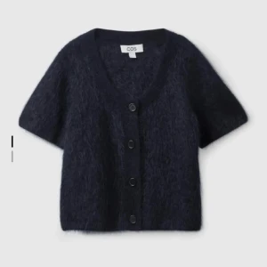 Mörkblå kofta från COS - Säljer en supermjuk och stilren mörkblå kofta från COS. Den har korta ärmar och knappar framtill, perfekt för lager-på-lager under hösten. Koftan är i ett fluffigt material som känns lyxigt och mysigt. Passar både till vardags och lite finare tillfällen!