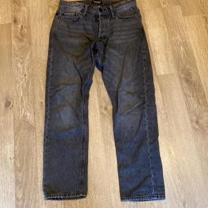 Grå jeans från Jack & Jones - Säljer ett par grå jeans från Jack & Jones i modellen Loose/Chris. De har en avslappnad passform och är perfekta för en casual look. Storlek 30:30Jeansen är i ny skick och har en klassisk femficksdesign med knappgylf. Perfekta för både vardag och avslappnade tillfällen.