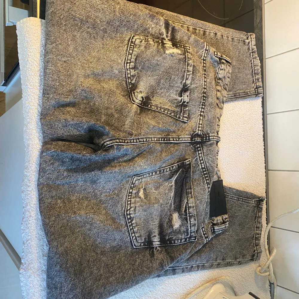 Säljer ett par grå jeans i nyskick med coola slitningar på framsidan. De har en klassisk femficksdesign och en knappgylf. Perfekta för en avslappnad stil och passar till det mesta. Storleken är normal och de är superbekväma att ha på sig.. Jeans & Byxor.