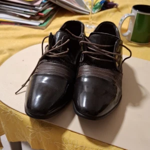 Bruna skor med snörning från Jingpin - Snygga bruna skor från Jingpin i nyskick. De har en glansig finish och snörning framtill. Perfekta för festliga tillfällen eller en stilren vardagslook. Skorna har en unik design med nätliknande detaljer på sidorna. Smala skor, storlek 37. Oanvända