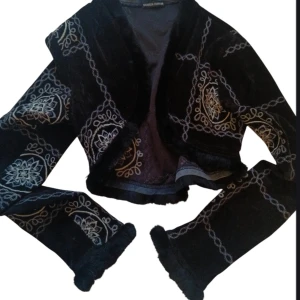 Svart sammet kavaj med broderi - Säljer en superfin svart kavaj i sammet från Claudia Chiffon. Den är croppad och har vackra broderade mönster i vitt. Perfekt för höst och vinter, och funkar både till fest och vardag. Ärmarna är långa och ger en elegant look. Passar perfekt till en kjol eller jeans!