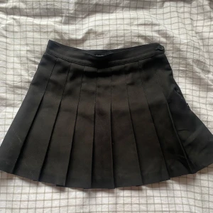 Svart tenniskjol - En svart kort tenniskjol från American Apparel! God kvalitet och använd några gånger, blixtlås och knapp i sidan. Storlek S men rätt liten så kanske bättre för XS! 