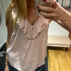 Rosa topp från Capri Collection - Säljer en söt rosa topp från Capri Collection i storlek S. Den har volangdetaljer runt halsen och är ärmlös, perfekt för sommardagar. Toppen är i ett lätt och luftigt material, vilket gör den bekväm att bära. Passar både till vardags och festliga tillfällen. 🌸pris går att diskutera!