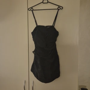 Kort klänning - Kort klänning omsydd från långklänning. Genomskinligt tyg (Meshtyg?) vid bröstet och bröstkorgen - se bild. Ej genomskinlig. Tight passform så anser att den sitter som 36 mer än 38. Kan användas utan axelbanden, vilka är justerbara. Dragkedja bak.