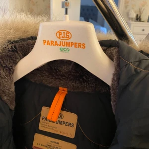 Parajumper Kodiak  - Svart dunjacka från Parajumpers. Praktiska och dekorativa detaljer, förstärkta armbågar, avtagbar hake i halsen, praktiska fickor varav en stängs med dragkedja. Flera innerfickor och dragkedjor nedtill i sidorna för justerbar passform. Luva med foder