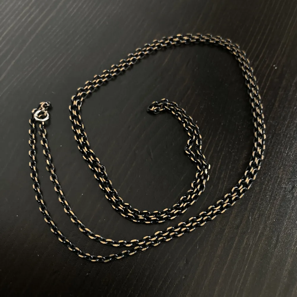 Långt halsband i svart och guldfärgad metall. Längd: 80 cm, bredd: 2 mm.. Accessoarer.