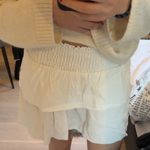 Vit kjol från Shein - Säljer en superfin vit kjol från Shein i storlek Petite XS. Den har en elastisk midja och volangdetaljer som ger en söt och luftig look. Perfekt för sommardagar. Knappt använd