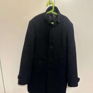 Riley Coat - Säljer en snygg svart kappa i ull med knappar fram. sparsamt använd och i 10/10 skick. Perfekt för höst och vinter, håller dig varm och snygg. Den har långa ärmar och en klassisk design som passar till allt. Ett måste i garderoben för den som gillar tidlös stil. 🖤​Nypris 2999