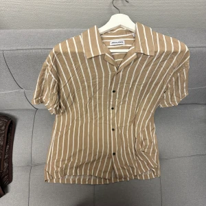 Beige och vit randig skjorta från Jack & Jones - Säljer en snygg beige skjorta med vita ränder från Jack & Jones. Aldrig använd. Strl:L.