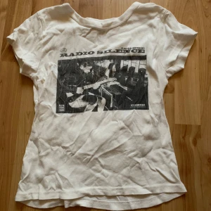Vit t-shirt med tryck från John Galt - Säljer en vit t-shirt från John Galt i storlek S. Den är gjord av 100% bomull och har ett coolt svart tryck med texten 'Radio Silence'. Perfekt för en avslappnad stil eller konsertkväll. Lite sliten men fortfarande i bra skick!