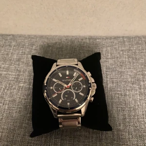 Silverfärgad klocka från Hilfiger - Stilren klocka från Hilfiger med silverfärgad metallarmband och svart urtavla. Klockan har tre mindre urtavlor och tydliga markeringar. Perfekt för en elegant look.