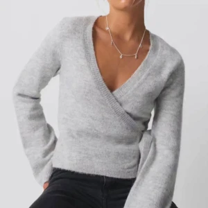 Grå omlottkofta med knytband - Säljer en stilren grå omlottkofta med knytband i mjukt material. Koftan har en v-ringad design och långa ärmar, perfekt för en avslappnad look. Från Gina tricot! 