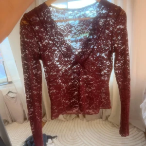 Vinröd spetsblus - Säljer en elegant vinröd spetsblus med lång ärm och v-ringning. Blusen är genomskinlig och har en tight passform, perfekt för en kväll ute, Har två små stora hål ❤️