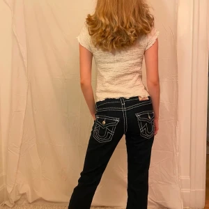 Blå true religion jeans med kontrastsömmar - Snygga blå jeans med vita kontrastsömmar . Jeansen har en normal passform.De har knappar och dragkedja framtill.