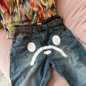 Jeans med tryck från BAPE - Unika jeans från BAPE med ett stort vitt tryck av ett ansikte på framsidan och diagonala ränder på bakfickan. Streetwear type denim blue jeans. Äktä och i jätte bra schick.