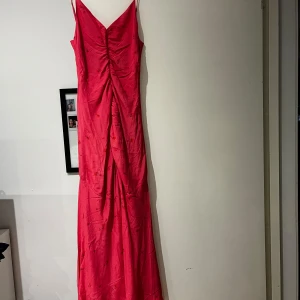 Röd långklänning från ADOORE - Elegant röd långklänning från ADOORE med smala axelband och v-ringning. Klänningen har ett subtilt blommönster och en figurnära passform som framhäver silhuetten. Perfekt för speciella tillfällen.