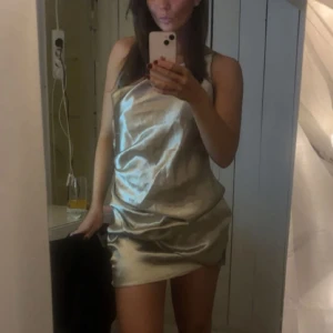 Champagnefärgad axelbandslös klänning - Elegant champagnefärgad axelbandslös klänning i satin. Perfekt för festliga tillfällen med sin glansiga yta och smickrande passform.