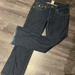 Mörkblå jeans från True Religion - Snygga mörkblå jeans från True Religion med klassisk femficksdesign och kontrasterande sömmar. Byxorna har en bootcut passform och är perfekta för en avslappnad stil. Märkeslogga på bakfickan ger en extra touch. Pris går att diskutera.