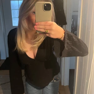 Svart knyttröja - Säljer en stilren svart omlottopp med långa ärmar. Toppen har en knytning i midjan som ger en smickrande passform. Perfekt för både fest och vardags. 