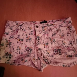 Blommiga shorts från H&M - Säljer ett par söta blommiga shorts från H&M i storlek 38 och är vita med ett färgglatt blommönster