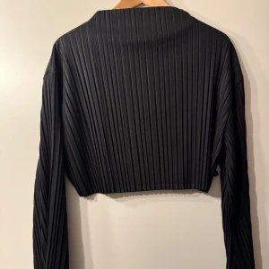 Svart croppad blus - Snygg svart croppad blus med ribbad struktur från Esthé. Långa utsvängda ärmar i en kortare modell. Passar superfint till middag eller fest 🕺 Utan anmärkningar. 