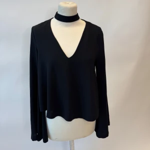 Svart långärmad topp med choker - Snygg svart långärmad topp med en djup v-ringning och inbyggd choker. Perfekt för en stilren och modern look.