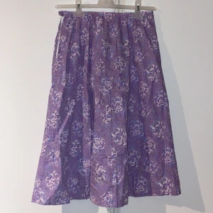 Lila blommig kjol - Lila kjol med ett vackert blommönster. Står ingen storlek på men skulle säga att den är ungefär som en xs (mått finns på bild 3).