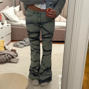 Grå mönstrade bootcut jeans - Snygga grå bootcut jeans med unikt mönster i svart. De har en lågmidjad passform och är perfekta för en trendig look. Säljer då de ej passade mig. Helt nya!! Säljer vid bra pris då jag är osäker 