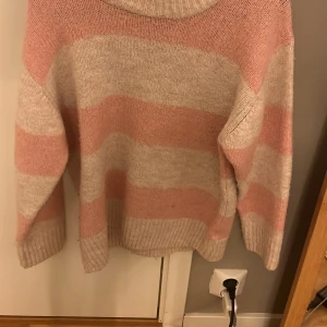 Rosa och beige/vit randig tröja från Gina Tricot - Mysig tröja från Gina Tricot i rosa och beige/vit med breda ränder. Den har en avslappnad passform och långa ärmar, perfekt för kyligare dagar. Ribbstickade muddar vid ärmslut och nederkant ger en skön känsla.