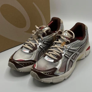 Asics GT-2000  - Snygga Asics GT-2000 sneakers i en kombination av silver, brunt och vitt. Skorna har snörning och en bekväm sula med bra grepp. Perfekta för löpning eller vardagsbruk.