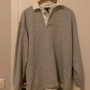 Grå pikétröja från H&M - Säljer en stilren grå långärmad  pikétröja från H&M i relaxed fit. Tröjan har en klassisk vit krage och knappar framtill. Perfekt för en avslappnad look. Priset kan dessutom diskuteras! 
