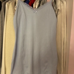 Blå klänning med spetsdetaljer - Snygg blå klänning med smala ränder och spetsdetaljer vid halsringningen. Perfekt för varma dagar eller som ett lager under en tröja. Har en liten rosett framtill🩵 knappt använd.