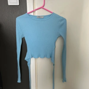 Blå ribbad croppad topp - Säljer en ljusblå ribbad croppad topp från New Yorker. Toppen har långa ärmar och en rund halsringning. Perfekt för en stilren och avslappnad look.
