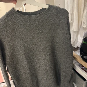 Grå stickad tröja från & Other Stories - Säljer en stilren grå stickad tröja från & Other Stories. Perfekt för kyligare dagar med sin mjuka och bekväma passform. Tröjan har en klassisk rund hals och ribbade detaljer vid hals och ärmslut.