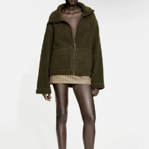 Olivgrön teddyjacka med dragkedja - Mysig olivgrön teddyjacka med dragkedja och hög krage. Perfekt för kyliga dagar med sin fluffiga textur och praktiska fickor framtill.