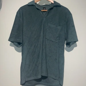 Grön frotté t-shirt från SOC - Tjena, säljer nu en riktigt snygg grön t-shirt i frotté från SOC med korta ärmar och en bröstficka. Den är riktigt skön att ha på sig och perfekt för en avslappnad stil.