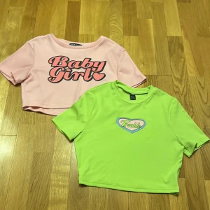 Två croppade toppar från Shein - Säljer två coola croppade toppar från Shein. Den ena är ljusrosa med texten 'Baby Girl' och den andra är limegrön med texten 'Trouble'. Båda topparna har korta ärmar och är ribbade för en trendig look. Perfekta för en avslappnad stil!